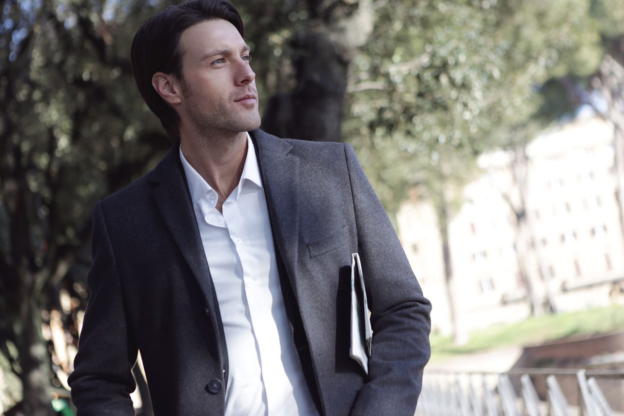 Elegant young man in formal attire standing outdoors, exuding confidence.